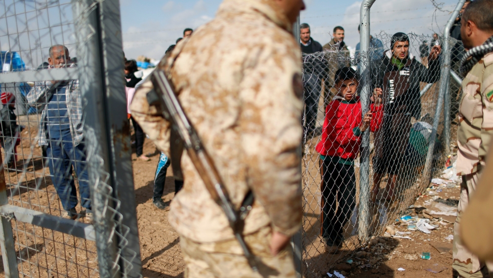 Displaced Iraqi people who fled from fighting Islamic State militants in Mosul, stand behind the fence at Khazer camp