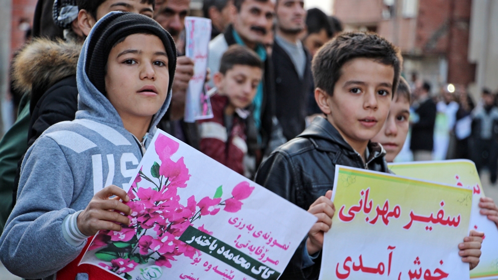 Two children awaiting Bakhtar in his hometown of Marivan held banners in Persian reading: 'Welcome messenger of kindness' [Dana Khormehr/Al Jazeera]