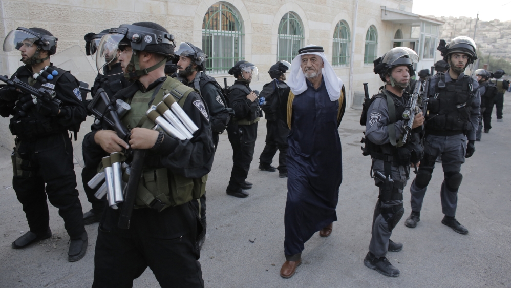 A man walks past Israeli police officers in Jabal Mukaber, near the home of a Palestinian suspected of an attack [Ammar Awad /Reuters]