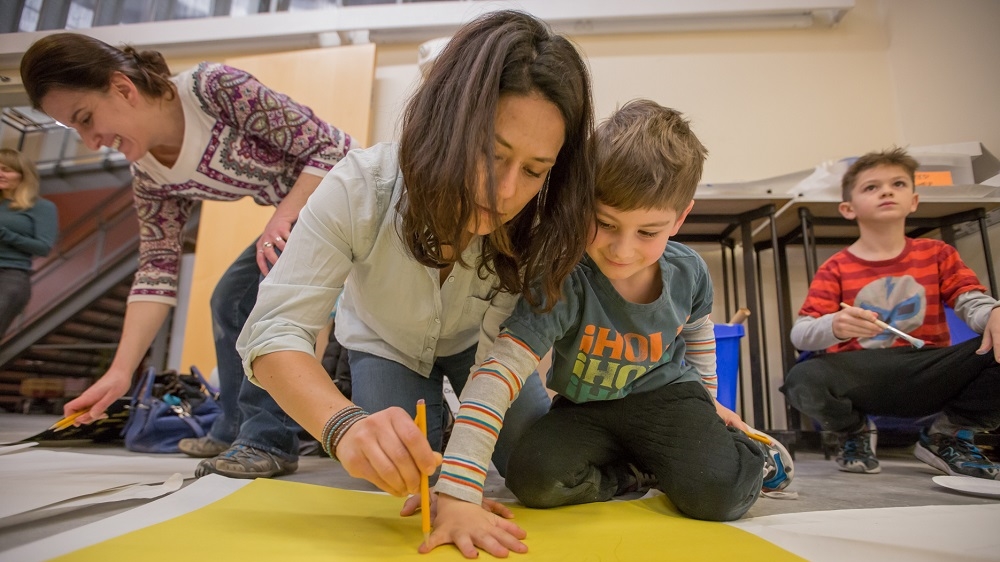 Natalia and one of her charges, Myles, draw their hands during a sign-making party for the We Are One Somerville rally [Carolyn Bick/Al Jazeera]