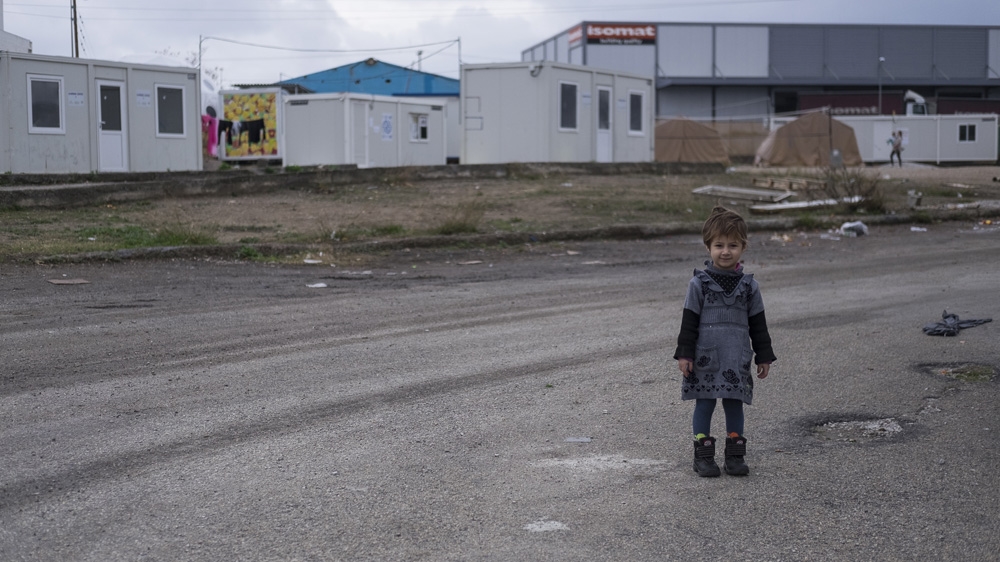 A young Afghan girl stands near the parking area at a camp in Oinofyta, a small town on the outskirts of Athens [Fahrinisa Oswald/Al Jazeera] 
