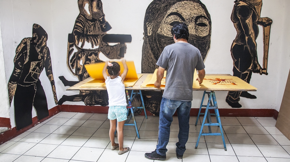 
Mario and his daughter count and sort screen prints for pasting on the city walls. Behind them, large wood prints depict images of protest [Gabriela Campos/Al Jazeera] 