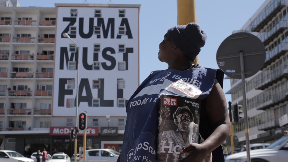 A Big Issue seller stands in front of a building reading