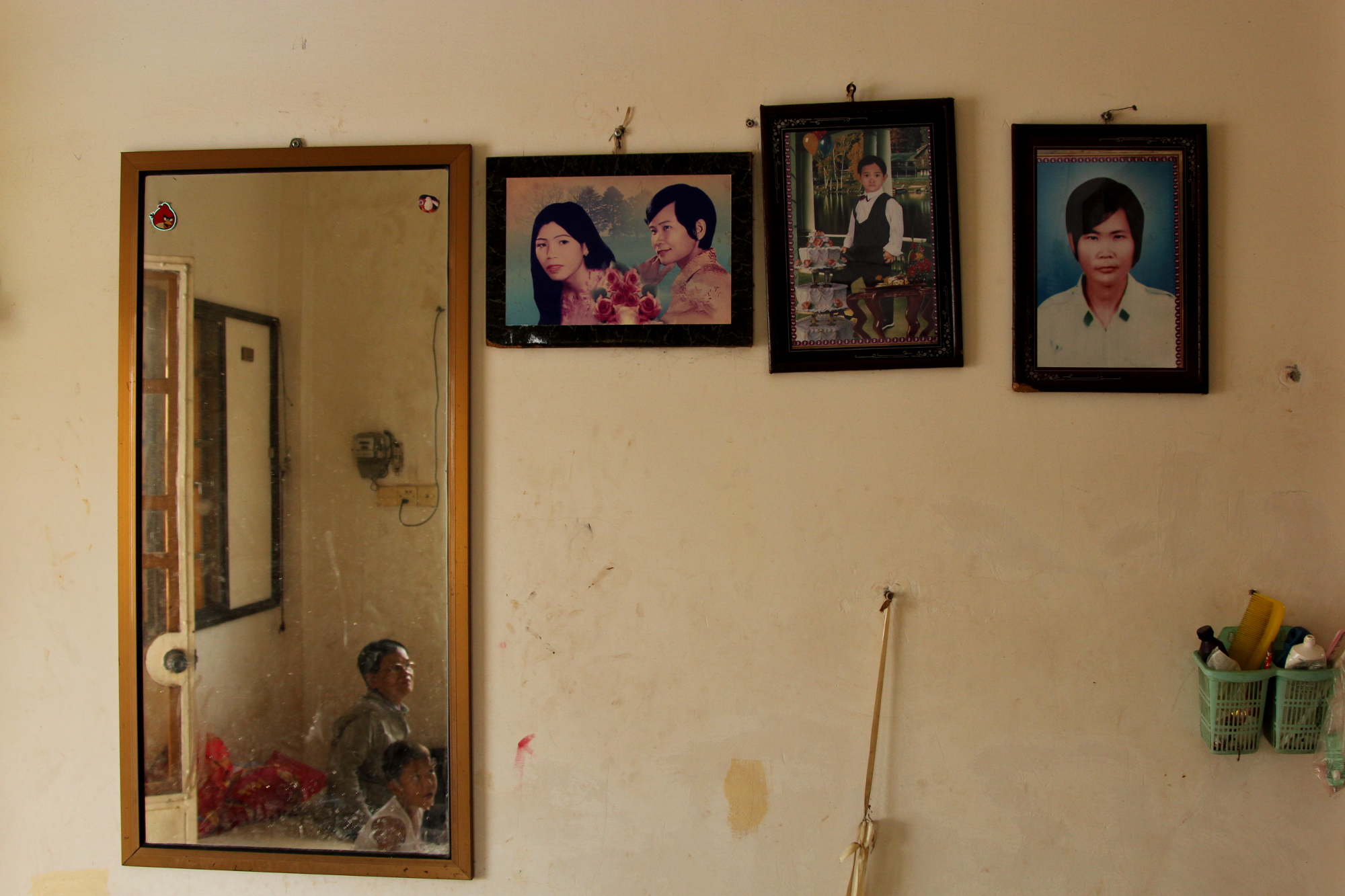 A photograph of Noy Sitha and Hong Saroeun, taken when they were in their 30s, hangs on the wall of their home. Next to it is a portrait of one of their grandsons, and to the far right, is a photograph of Noy Sitha [Laura Villadiego/Al Jazeera]