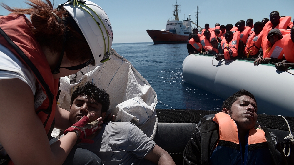 A rescuer helps migrants from an overcrowded plastic raft that was drifting during a search and rescue operation by rescue ship Aquarius, operated by SOS Mediterranean and Doctors without Borders