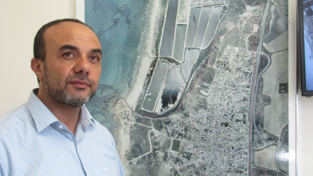 Murad Amash stands beside a map of Jisr al-Zarqa, which is surrounded by wealthy Jewish towns [Yuval Abraham/Al Jazeera] 