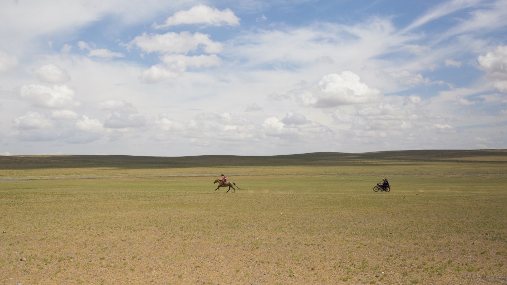 Damdinsuren sprints her horse on a final training ride before a 24km race the next day. Her father and older sister, both former horse racers, follow on a motorcycle [Hannah Griffin/Al Jazeera]