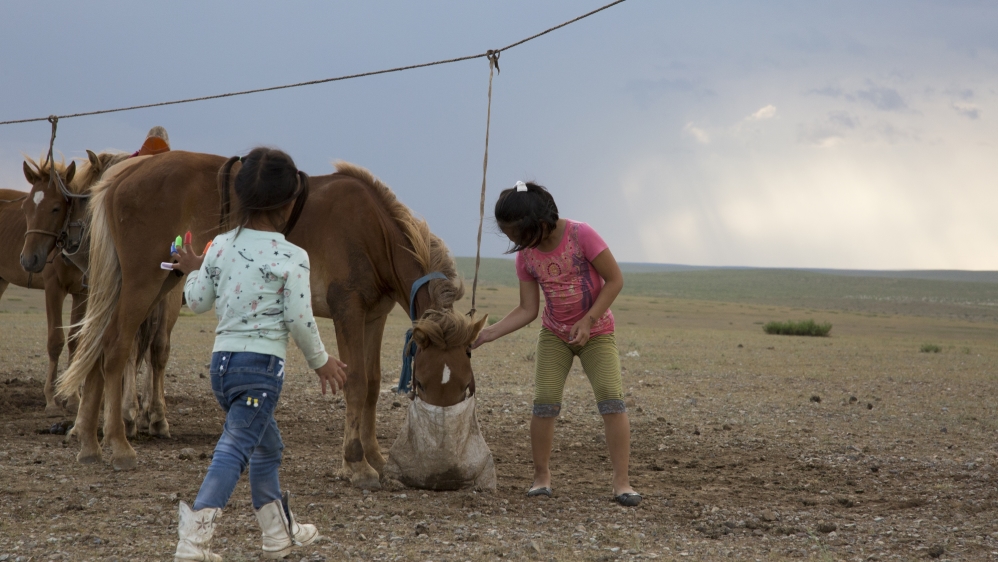 Bujinlkham Damdinsuren and her sister Yanjinlkham feed their family’s horses [Hannah Griffin/Al Jazeera]