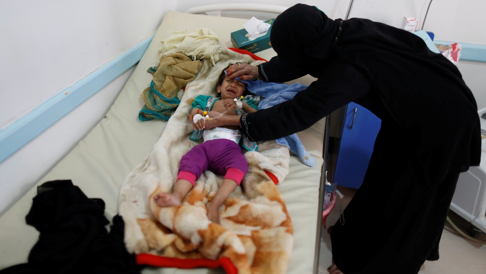 Woman helps her son as he lies on a bed at a cholera treatment center in Sanaa, Yemen