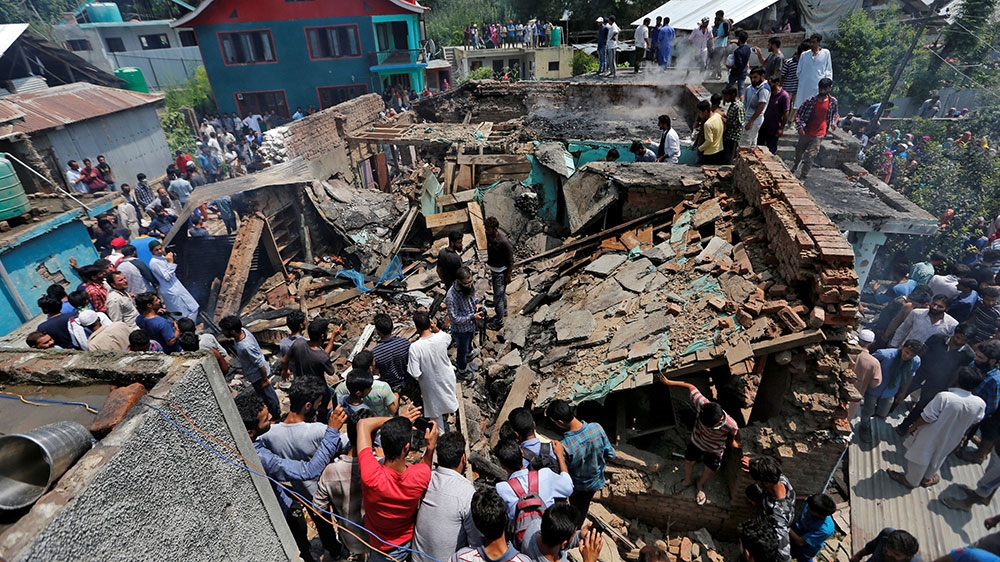People stand on the rubble of a house after it was damaged during a gun battle between fighters and Indian security forces in Hakripora in south Kashmir's Pulwama district [Danish Ismail/Reuters]