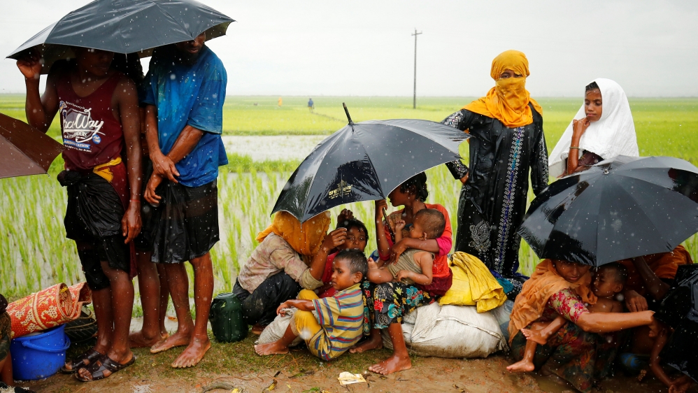 Rohingya refugees with children sit in the open during heavy rain as they are held by Border Guard Bangladesh [Mohammad Ponir Hossain/Reuters]