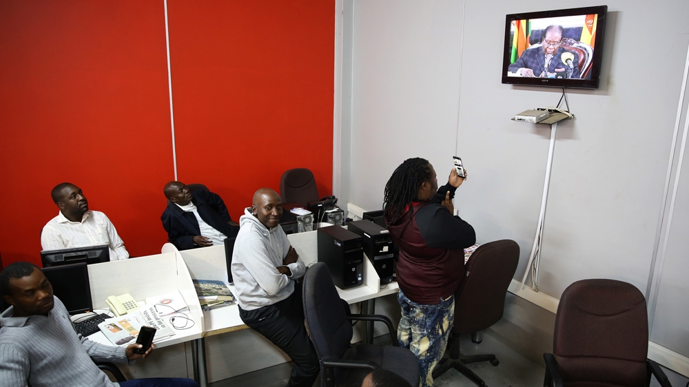 A group of workers watch as Mugabe addresses the nation [Aaron Ufumeli/EPA]