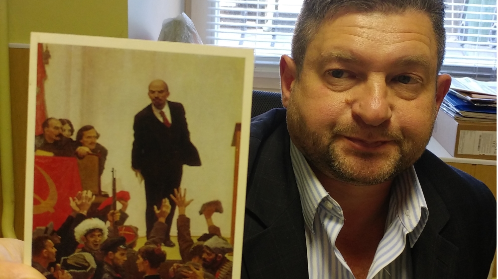 Anton Antonov-Ovseenko holds up a reproduction of a Soviet poster which features his grandfather, Vladimir Antonov-Ovseenko (to the left of Lenin). After he was arrested in 1938, his image was removed from the official poster [Mariya Petkova/Al Jazeera]