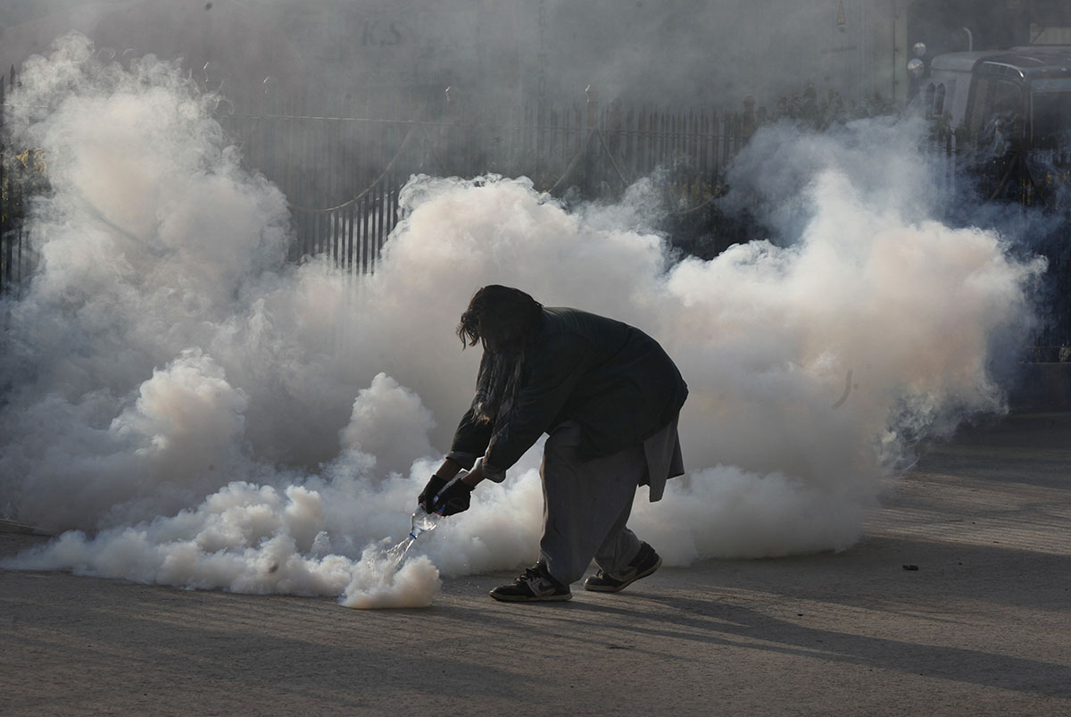 A protester pours water on a tear gas shell fired by police during a clash in Islamabad, Pakistan, Saturday, Nov. 25, 2017. Pakistani police have launched an operation to clear an intersection linking