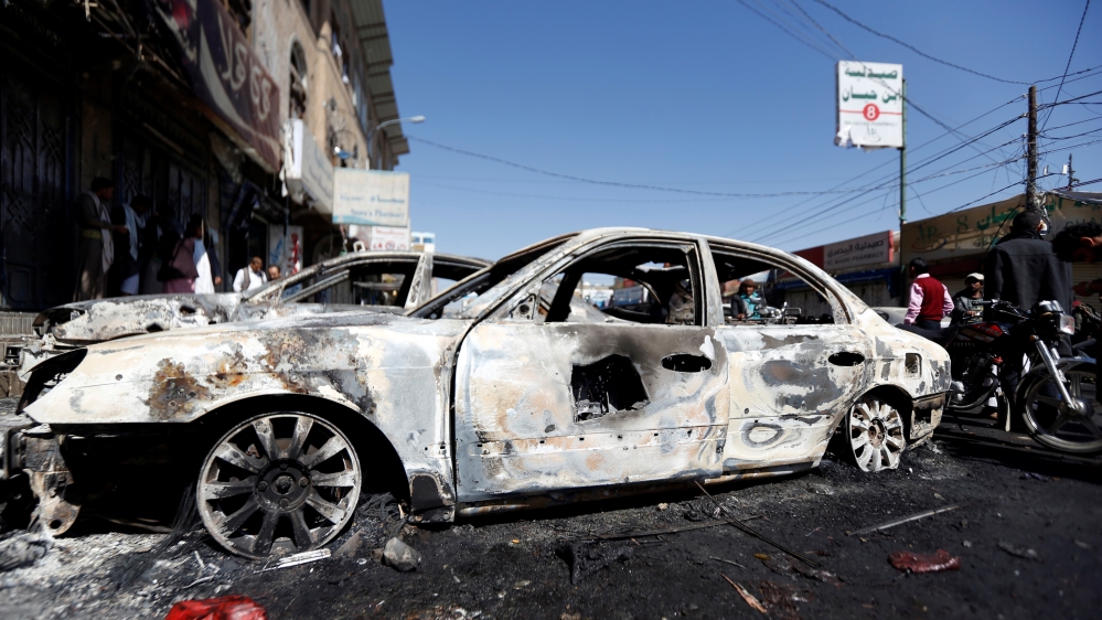 People go about their day near cars damaged during recent clashes between Houthi fighters and forces loyal to Yemen''s former president Ali Abdullah Saleh in Sanaa, Yemen