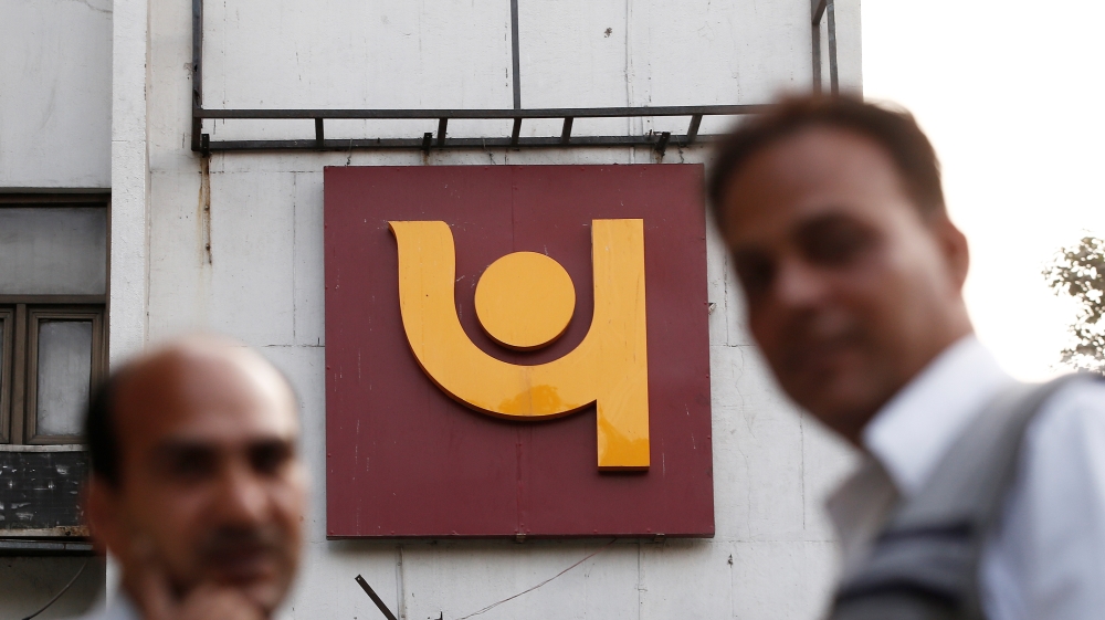 People stand in front of the logo of Punjab National Bank outside a branch of the bank in New Delhi