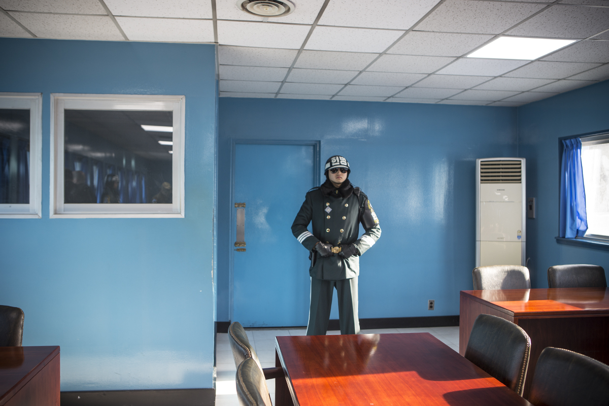 Inside the conference room – half of which is on North Korea’s side of the MDL – a soldier stands guard by the door that leads to North Korea. The taekwondo pose and dark shades form a military proced