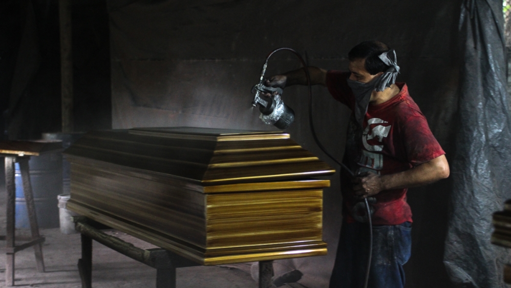 A worker applies sealant to a coffin at a factory in Jucuapa [Ali Rae/Al Jazeera]