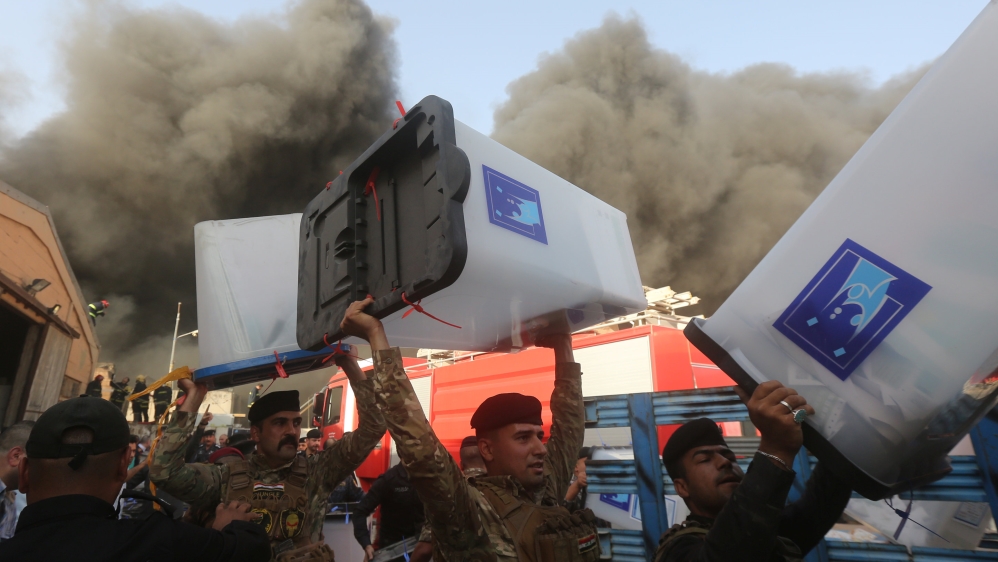 Security forces carry ballot boxes as smoke rises from a storage site in Baghdad, housing the boxes from Iraq''s May parliamentary election
