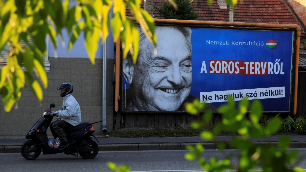 A man rides his moped past a government billboard displaying George Soros in monochrome next to a message urging Hungarians to take part in a national consultation about what it calls a plan by the Hu