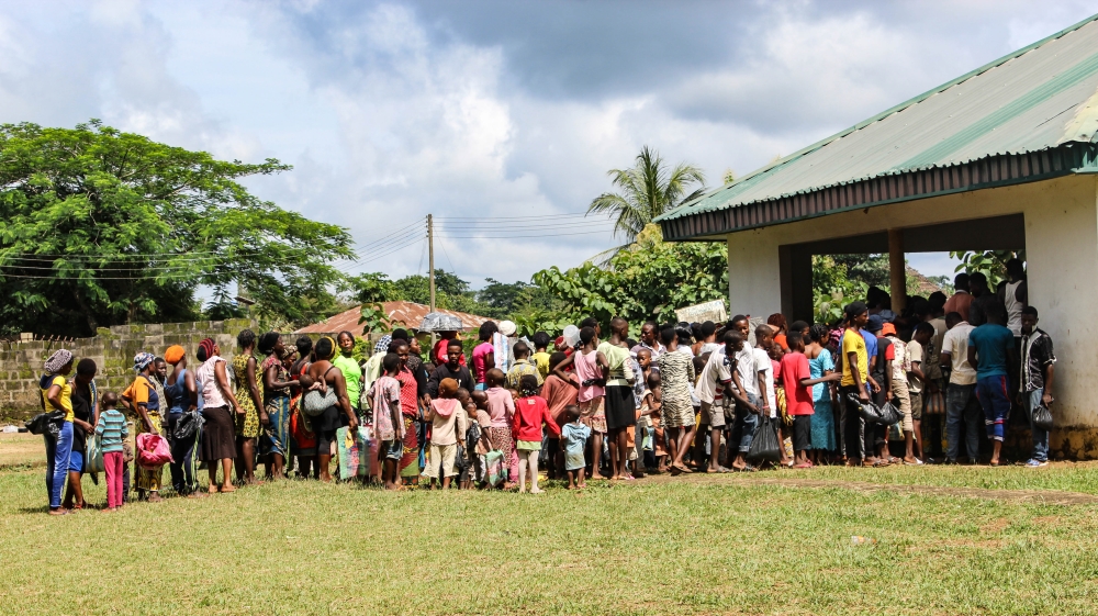 Cameroonian refugees in Agbokim Waterfall village wait in the sweltering heat outside a centre to receive assistance [Linus Unah/Al Jazeera]