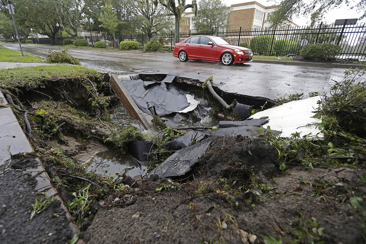 A car travels past a sinkhole in downtown Wilmington, N.C., after Hurricane Florence traveled through the area Sunday, Sept. 16, 2018. (AP Photo/Chuck Burton)