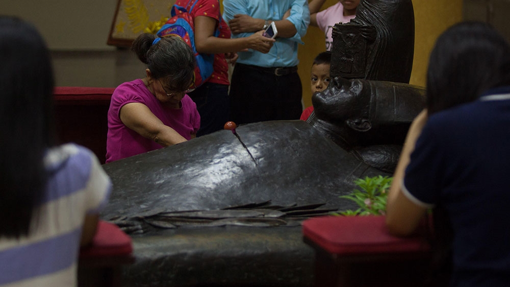 A woman prays at the crypt of Oscar Romero in the National Cathedral of San Salvador [Jeff Abbott/Al Jazeera] 