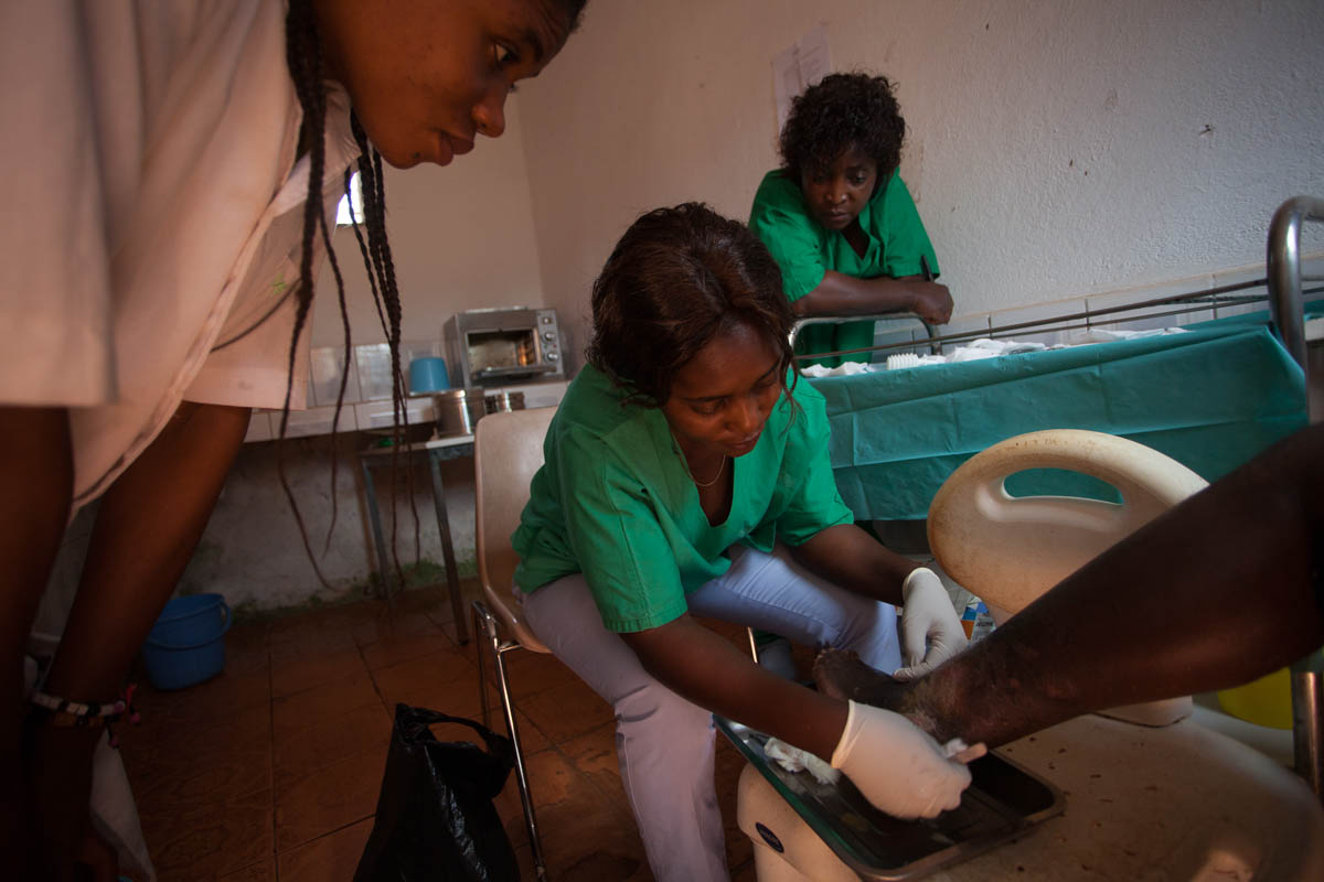 Mireille and Chantale change the dressing of Désiré Noutinou, 62 years old, under the attentive eye of Vicky, intern at the Hospital for a month.