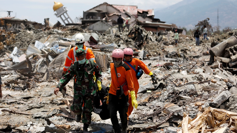 Rescue workers and a soldier remove a victim of the September 28 earthquake from the Balaroa neighbourhood of Palu [Darren Whiteside/Reuters]
