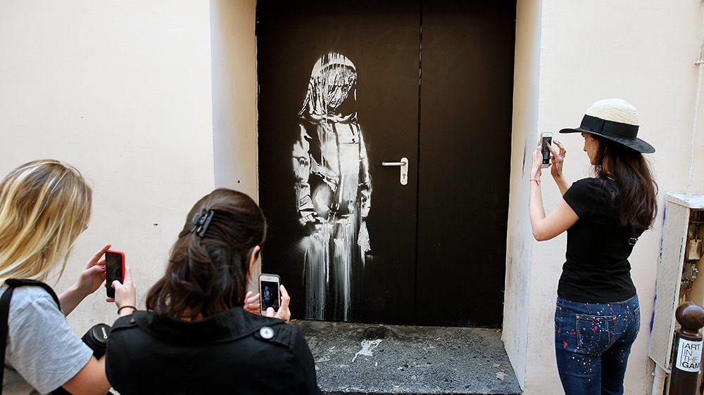 Young women take a picture of a recent artwork attributed to street artist Banksy on June 26, 2018 in Paris,