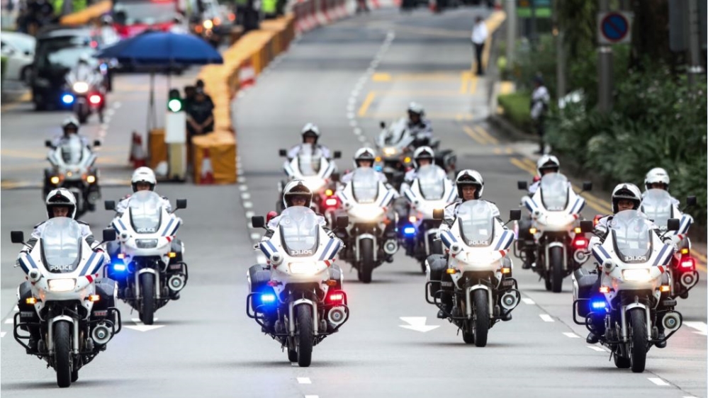 Police officers lead Kim's motorcade heading to Capella Hotel [File: Yong Teck Lim/AP Photo]
