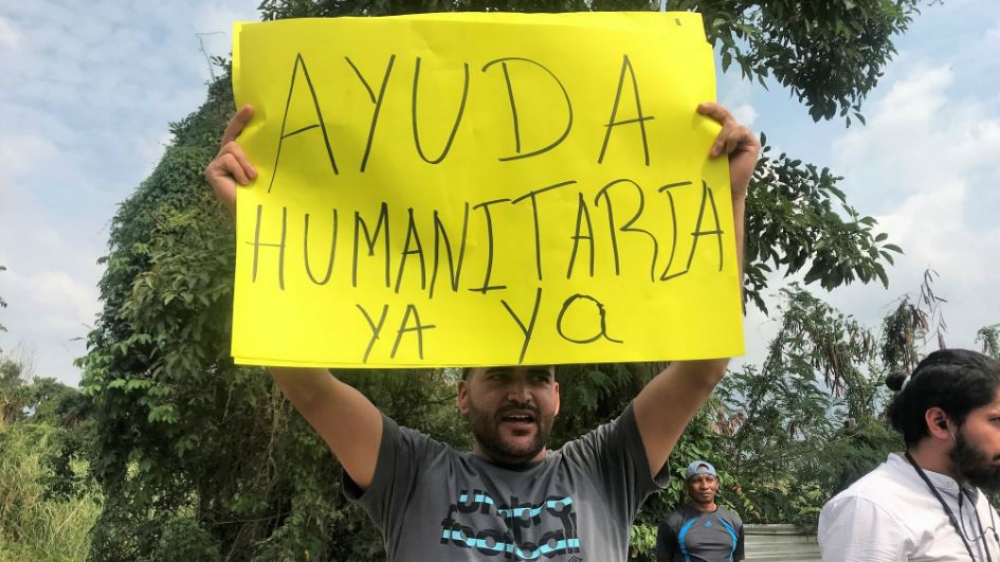 Luigi Rivas holds a sign reading 'humanitarian aid now' at the Tienditas border bridge [Steven Grattan/Al Jazeera]