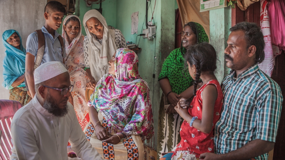 Bushra Shamnad, centre, talks to neighbours about her husband’s experience of migration. Pokkoya Shamnad (right, holding his seven-year-old daughter), moved to Kuwait in 2013. He was abused by his employer and returned a year later without receiving any pay [Sebastian Castelier/Al Jazeera]