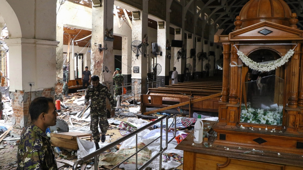 Sri Lankan security personnel walk past dead bodies covered with blankets amid blast debris at St Anthony's Shrine [Ishara S Kodikara/ AFP]