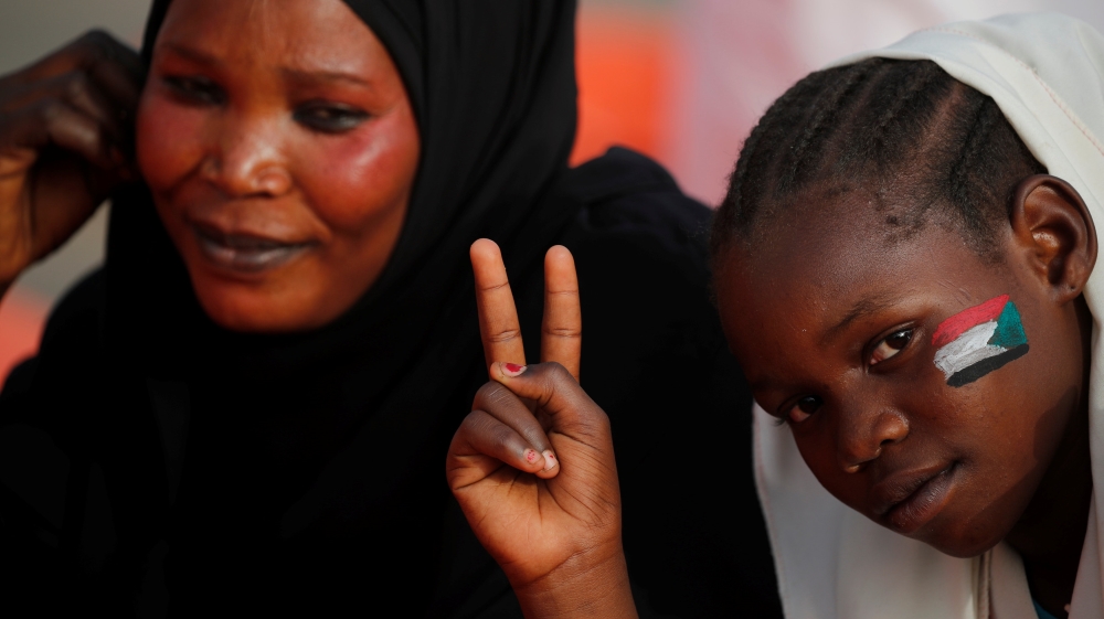 A girl with a painted Sudanese flag on her face makes victory sign as she is accompanied by her mother in front of the Defence Ministry in Khartoum [Umit Bektas/Reuters]