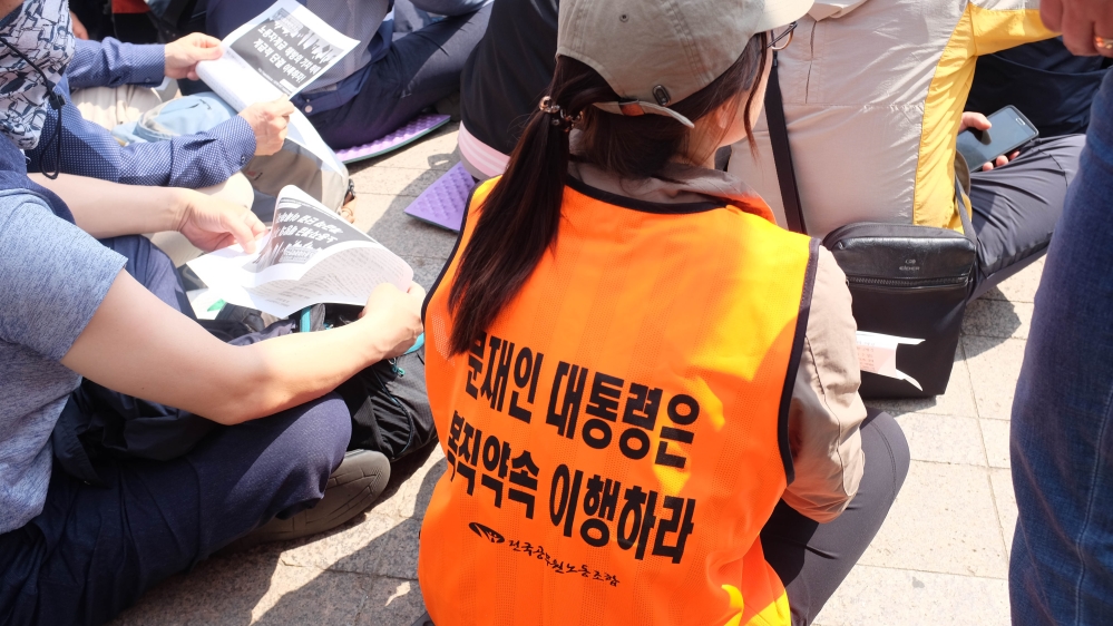 A demonstrator wears an orange vest with 'Moon Jae-in, keep the promise to reinstate' written on it [Sookyoung Lee/Al Jazeera]