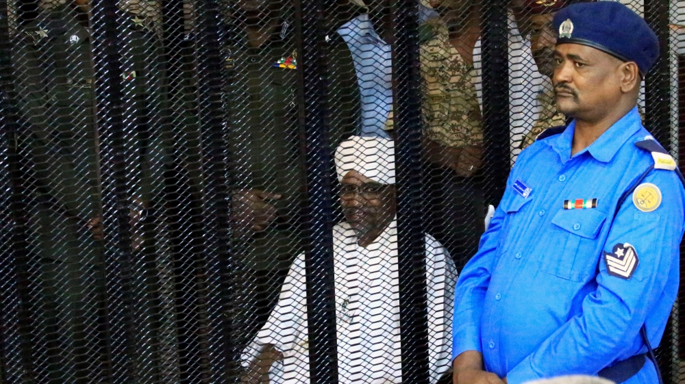 Sudan''s former president Omar Hassan al-Bashir sits guarded inside a cage at the courthouse where he is facing corruption charges, in Khartoum