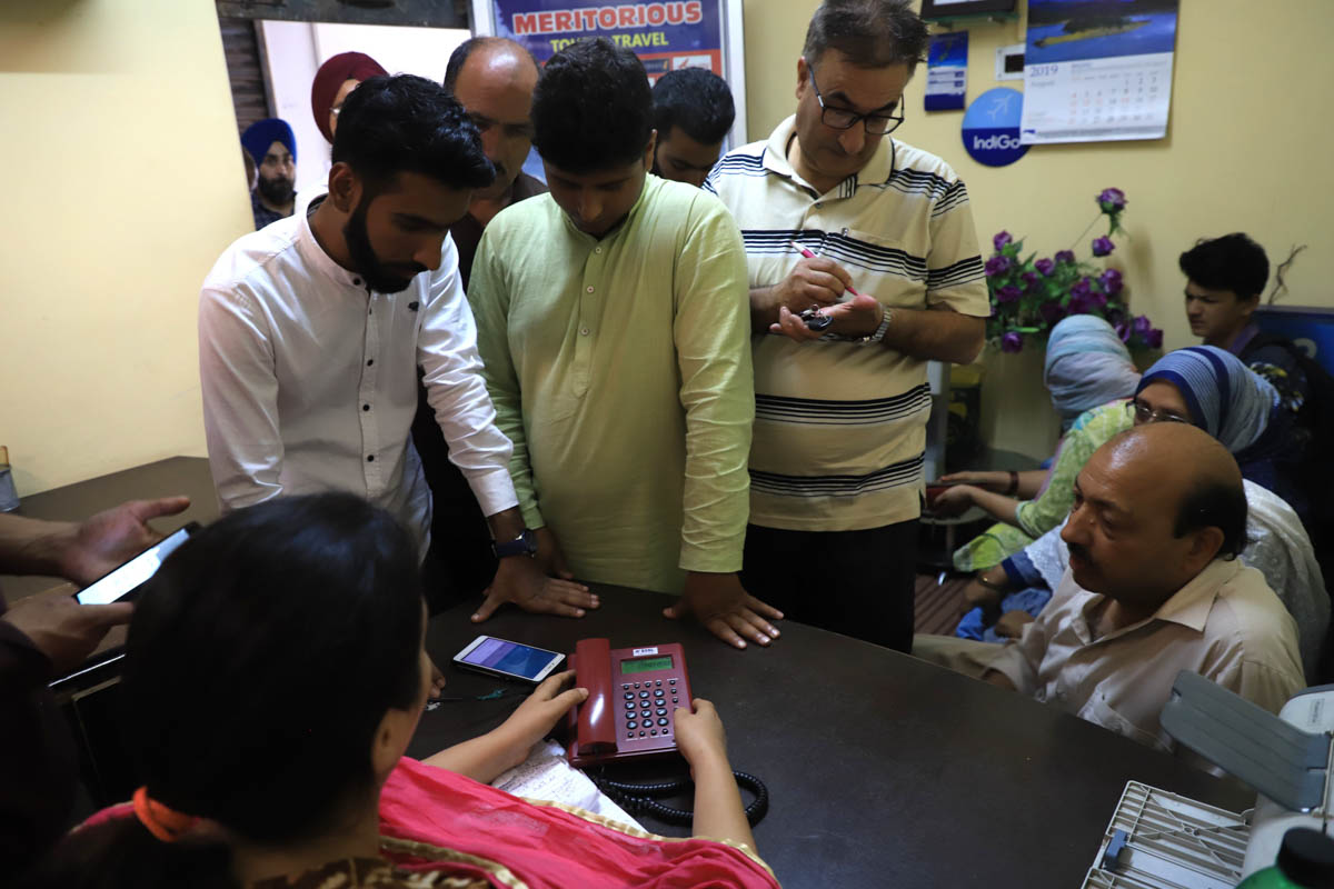 People wait to make calls at A voluntary temporary telephone booth setup in times of communication blackout in Rajbagh area of Srinagar on August,24 ,Yasmeen the owner of the space (Travel agency) say