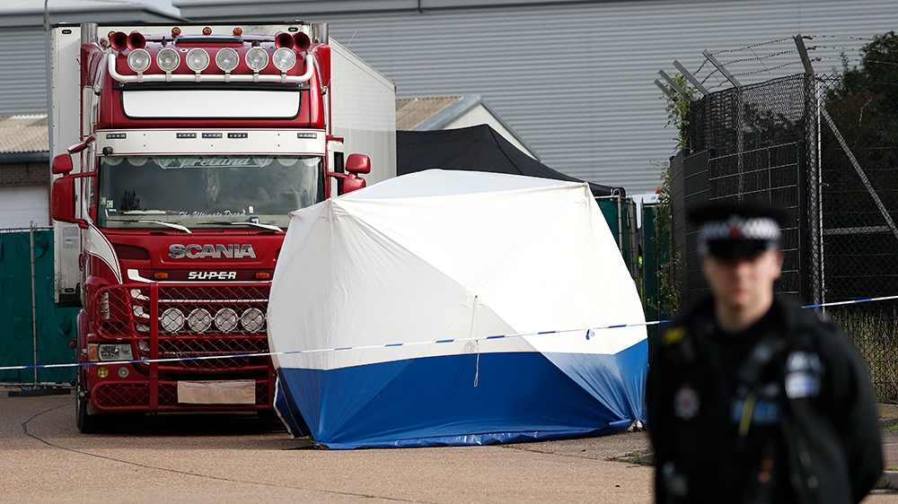 A police officer stands guard in front of a truck, in rear, that was found to contain a large number of dead bodies, in Thurrock, South England, early Wednesday Oct. 23, 2019. Police in southeastern E