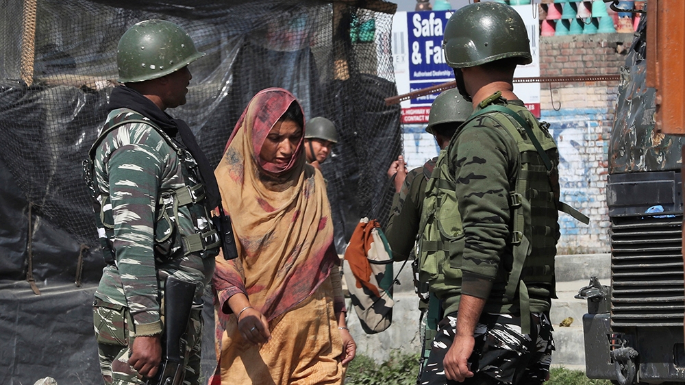 Indian paramilitary soldier guard as a Kashmiri villager woman walks near the site of gun-battle in south of Srinagar, Indian controlled Kashmir, Wednesday, Oct. 16, 2019. (AP Photo/Mukhtar Khan)
