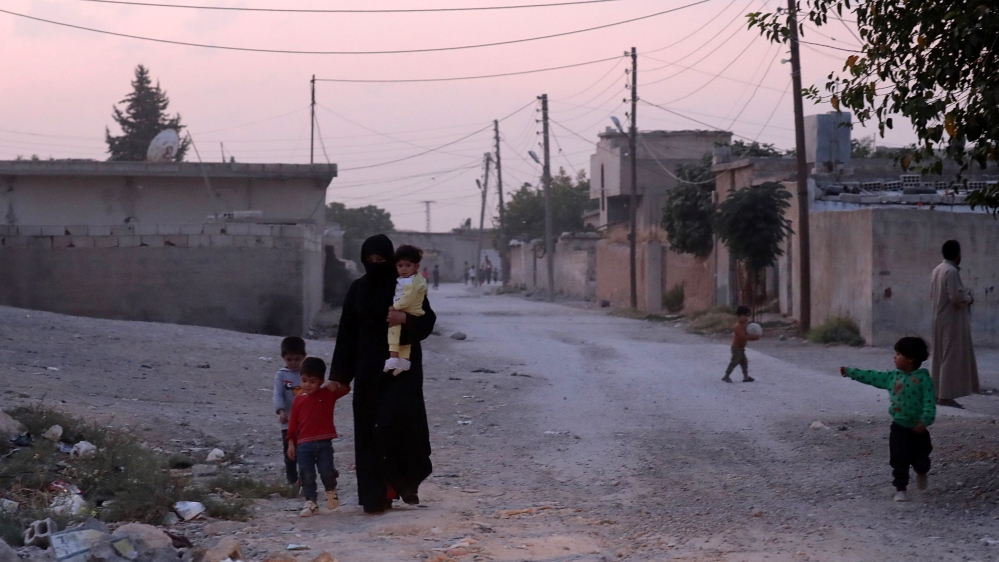 A woman holds a child as she walks along a street in the border town of Tal Abyad