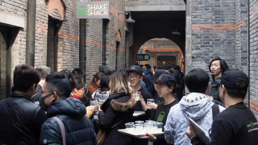 Staff members give out drinks to customers who are queuing for the newly opened U.S. burger chain Shake Shack restaurant in Shanghai