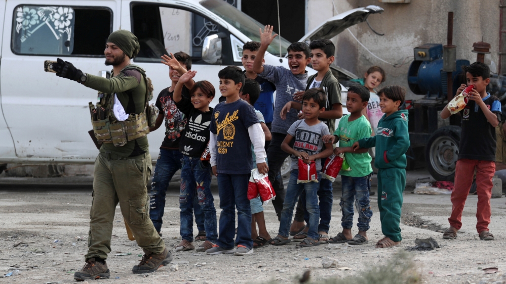 A Turkey-backed Syrian rebel fighter takes a picture with with children on his mobile phone in the border town of Tal Abyad