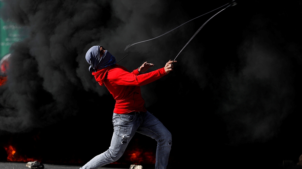 A demonstrator hurls stones at Israeli troops during a protest as Palestinians call for a day of rage over U.S. decision on Jewish settlements, near the Jewish settlement of Beit El in the Israeli-occ