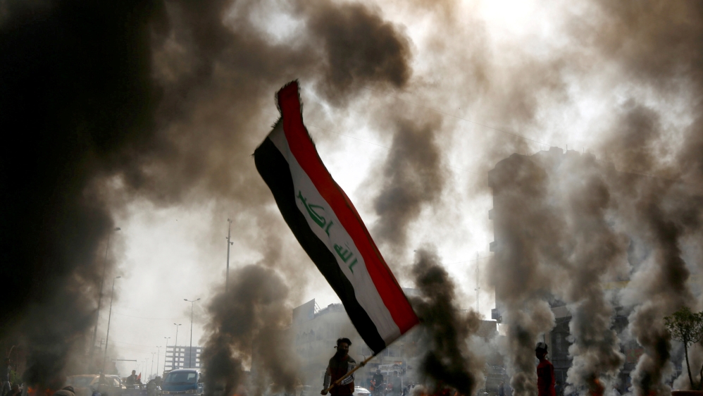 FILE PHOTO: A protester holds an Iraqi flag amid a cloud of smoke from burning tires during ongoing anti-government protests in Najaf, Iraq November 26, 2019. REUTERS/Alaa al-Marjani/File Photo