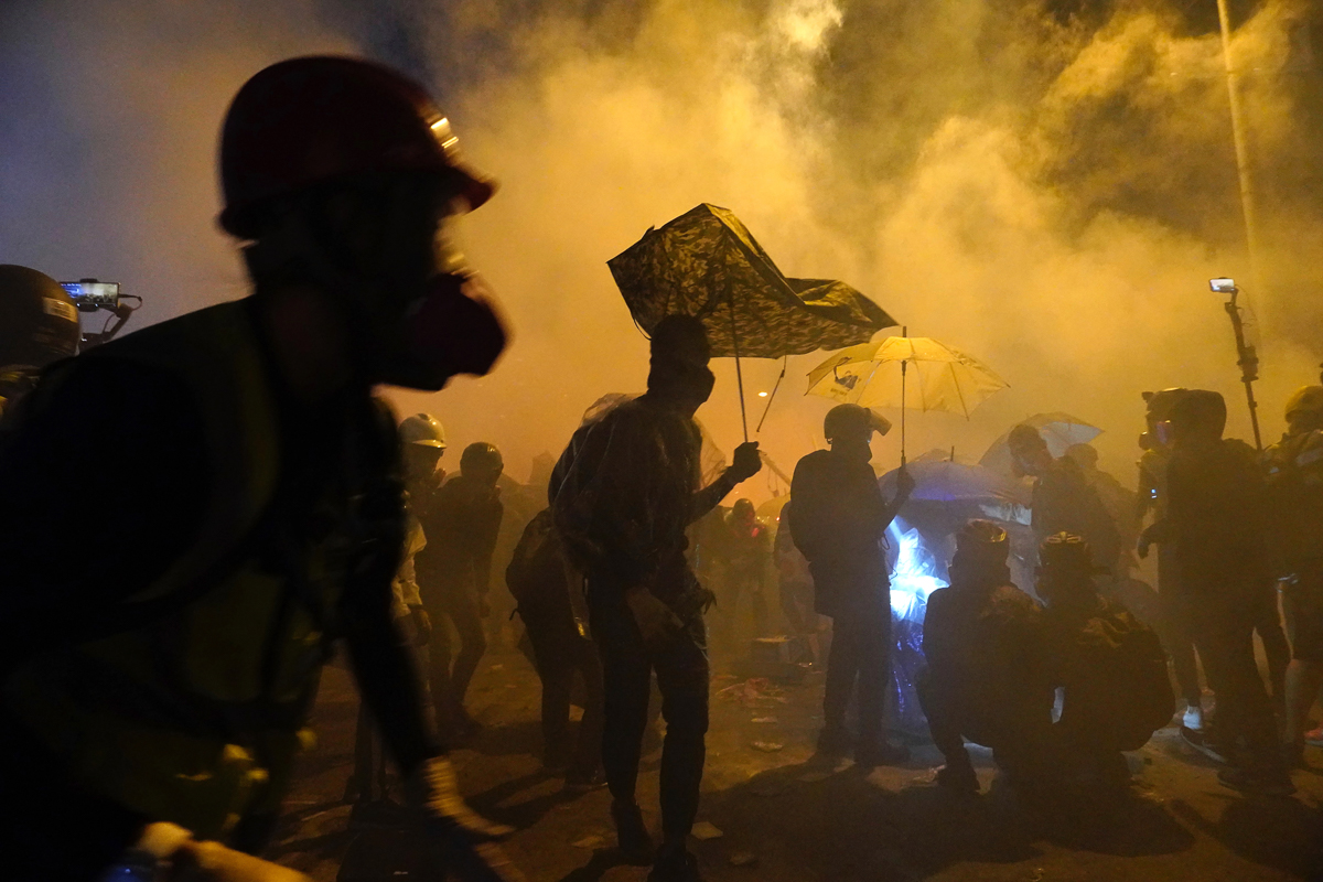 Protestors stand amid smoke on a bridge over a highway leading to the Cross Harbour Tunnel in Hong Kong, Sunday, Nov. 17, 2019. A Hong Kong police officer was hit in the leg by an arrow Sunday as auth
