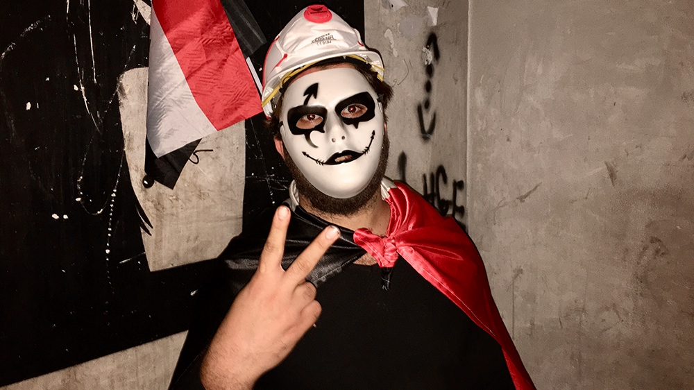 a man in a guy fawkes mask stands on the landing of the dark stairway leading up the tower [Sofia Barbarani/Al Jazeera]