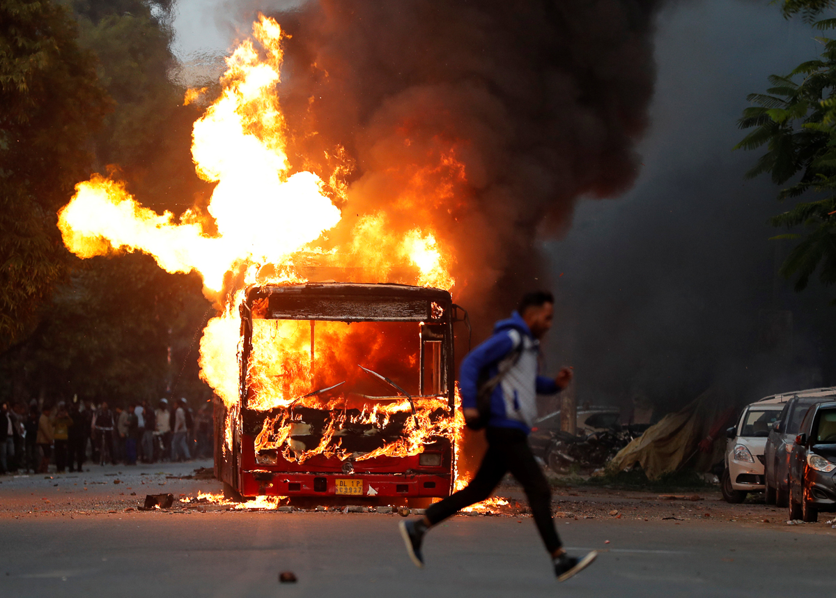 A man runs past a burning bus that was set on fire by demonstrators during a protest against a new citizenship law, in New Delhi, India, December 15, 2019. REUTERS/Adnan Abidi
