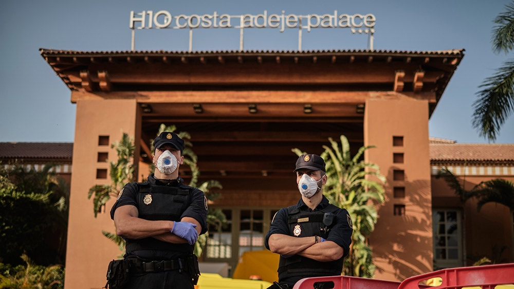 Police officers wearing masks stand in front of the H10 Costa Adeje Palace hotel in La Caleta, in the Canary Island of Tenerife, Spain, Wednesday, Feb. 26, 2020. Spanish officials say a tourist hotel