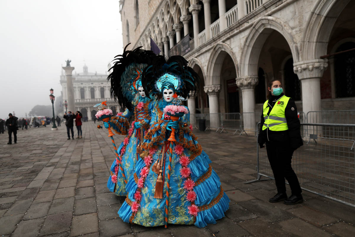 A policewoman wearing a protective mask stands next to carnival revellers at Venice Carnival, which the last two days of, as well as Sunday night's festivities, have been cancelled because of an outbr